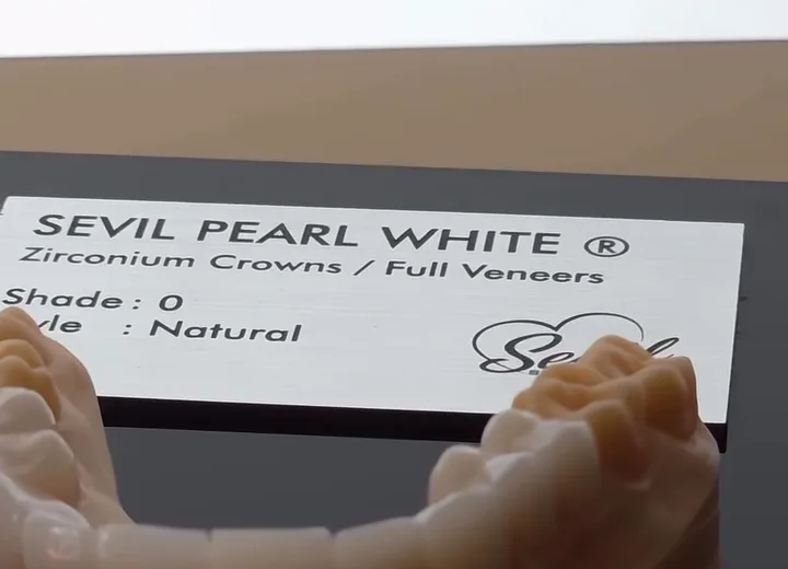 A zirconia bridge on the bench beside its printed specification card naming the material and a natural shade